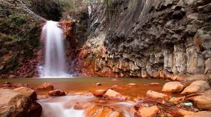 Pulangbato Falls pouring between red cliffs into an orange-tinted stream