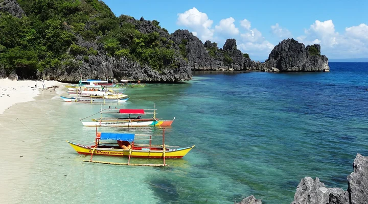 Outrigger boats on a white beach between limestone cliffs, Caramoan
